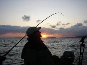 An angler in silhouette trolling for salmon.