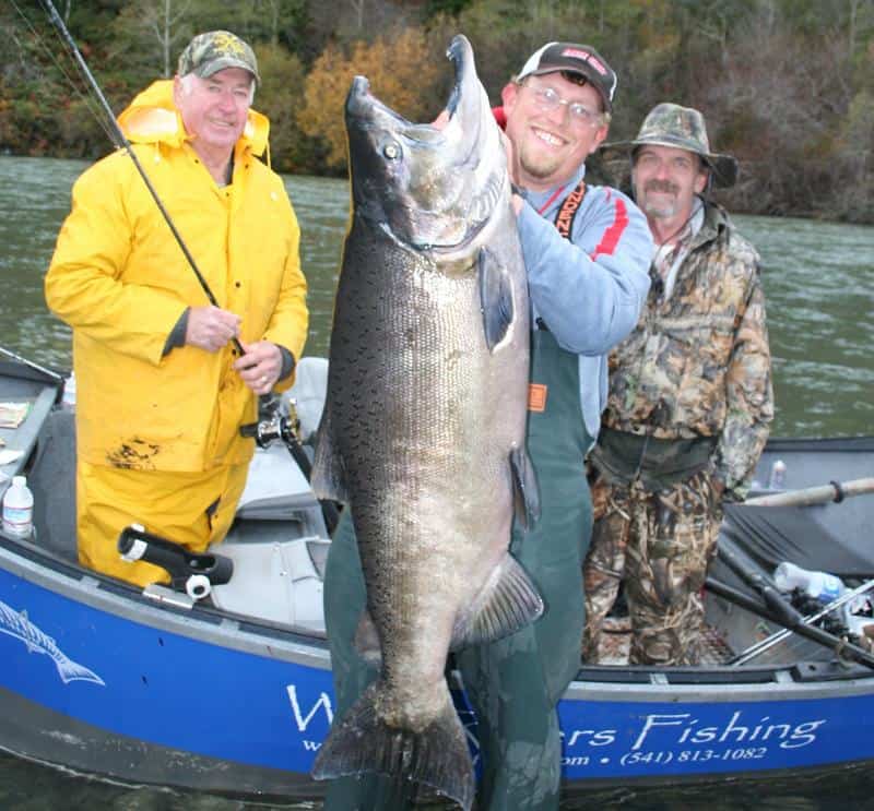 Anglers showcasing a massive chinook salmon caught in oregon.
