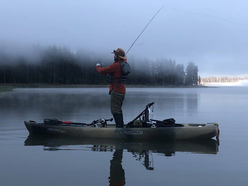 An angler fly fishing on a boat for largemouth bass with a scenic view of davis lake behind.