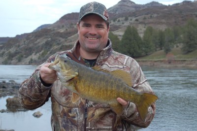 An angler holding a fish with a view of john day river behind.