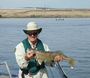 An angler showcasing a fish with a lake behind.