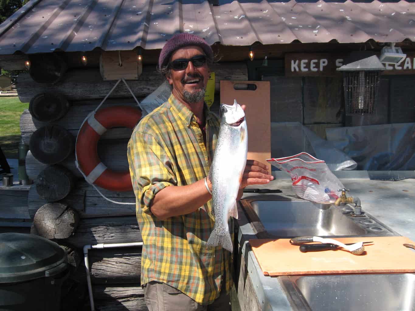 An angler holding a rainbow trout beside the cleaning station.