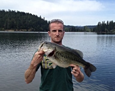 An angler holding a largemouth bass with a scenic view of selmac lake behind.