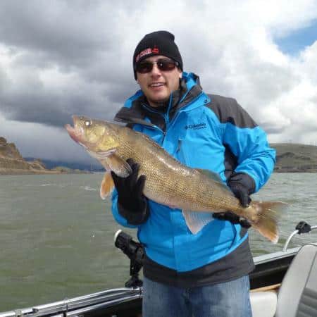 An angler holding a fish with a lake behind.