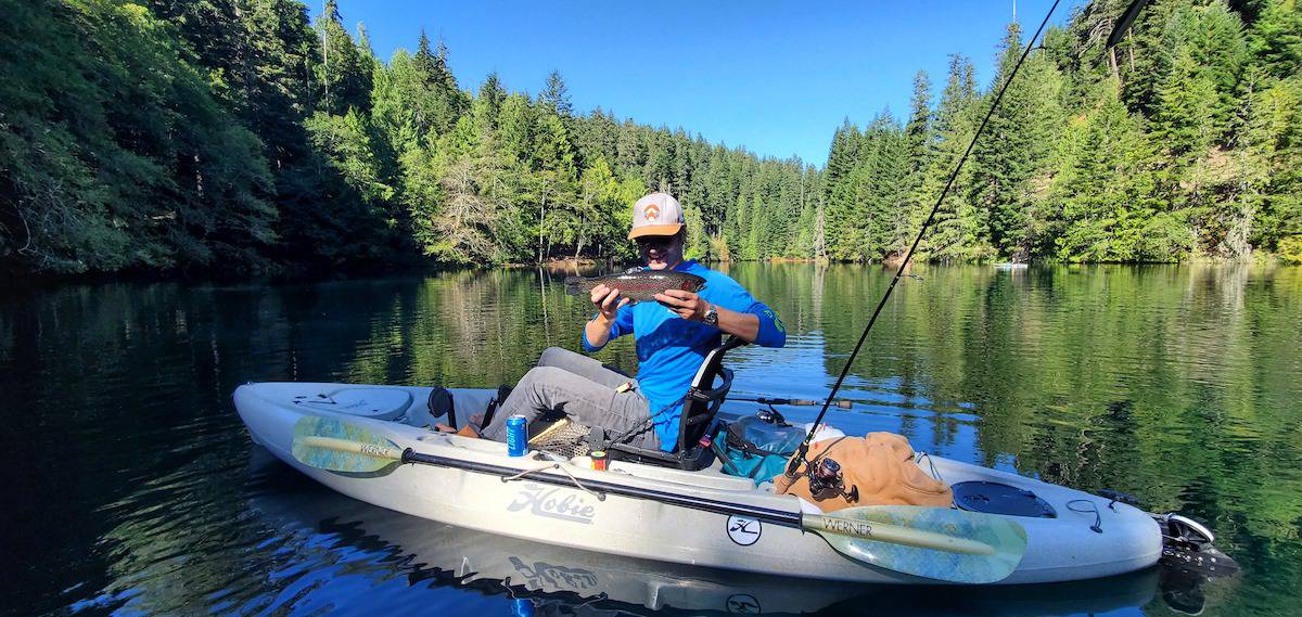 An angler in a kayak holds up a trout caught in Harriet Lake.