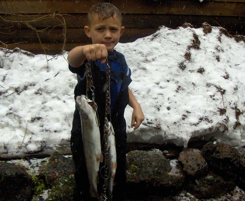 A kid holding a fish with snow behind.