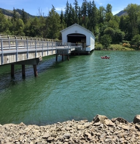 A scenic view of the covered bridge at Dexter Reservoir with a kayaker paddling through prime fishing water.