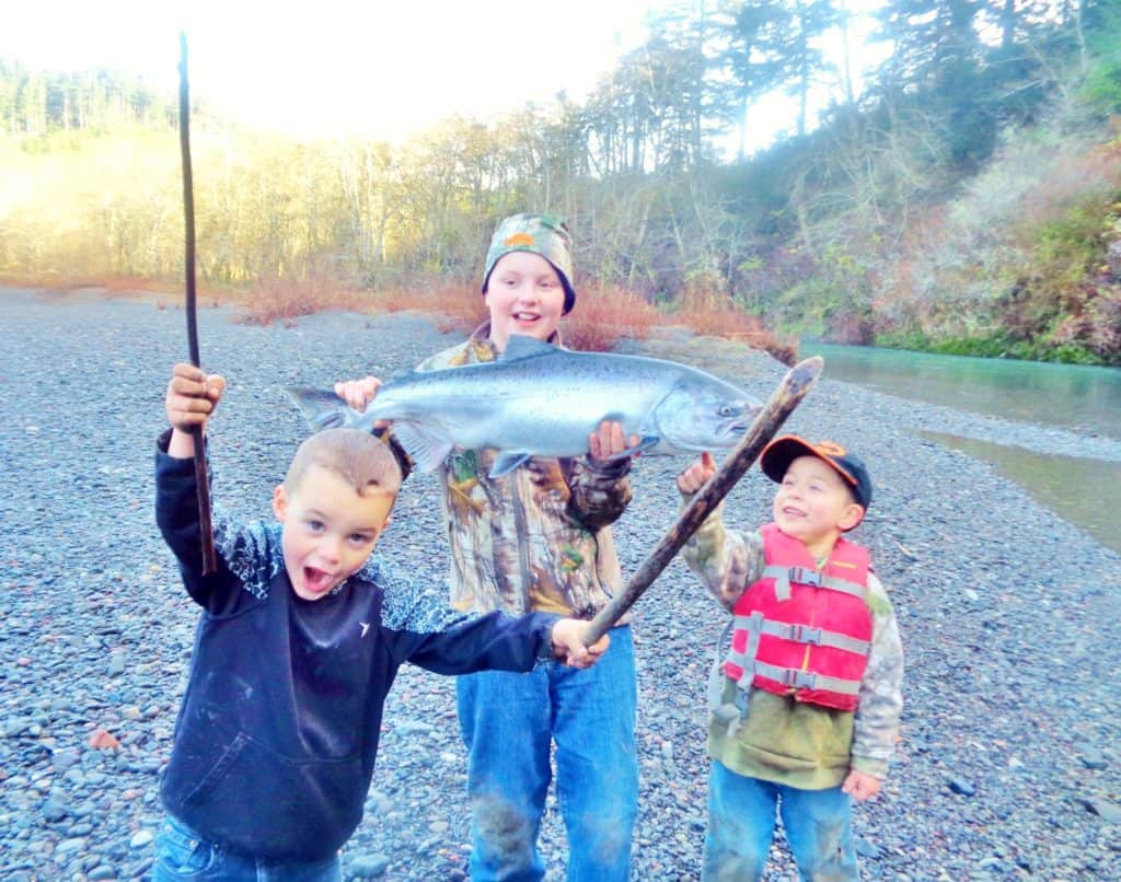 Three kids showcasing their caught salmon at sixes river.