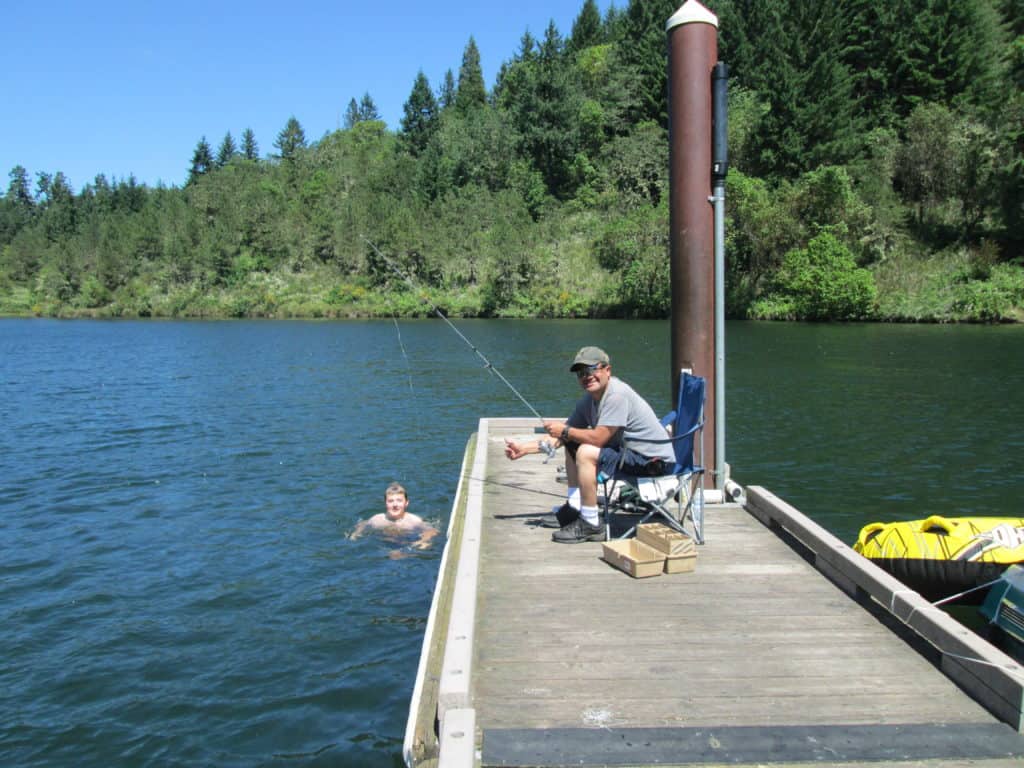 A man fishes from the dock at Cooper Creek Reservoir while another person swims.