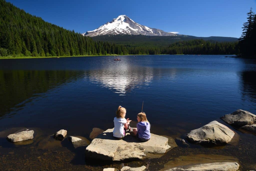 Kids sit on a big rock while fishing at trillium lake Oregon.