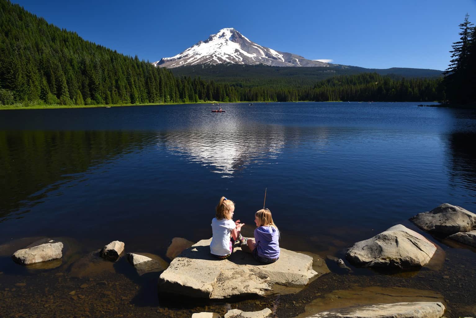 Two anglers sitting with a scenic view of trillium lake in the background.