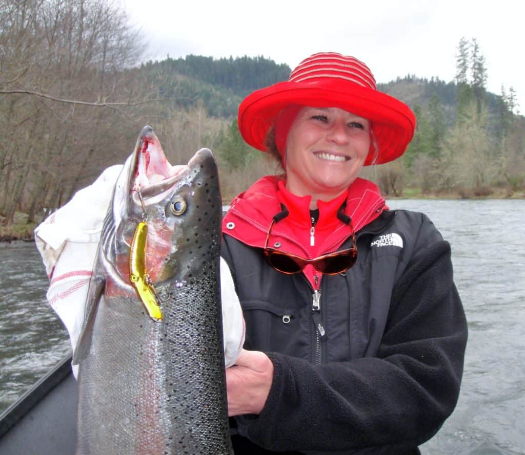 A woman angler holding a large steelhead caught in the rogue river.