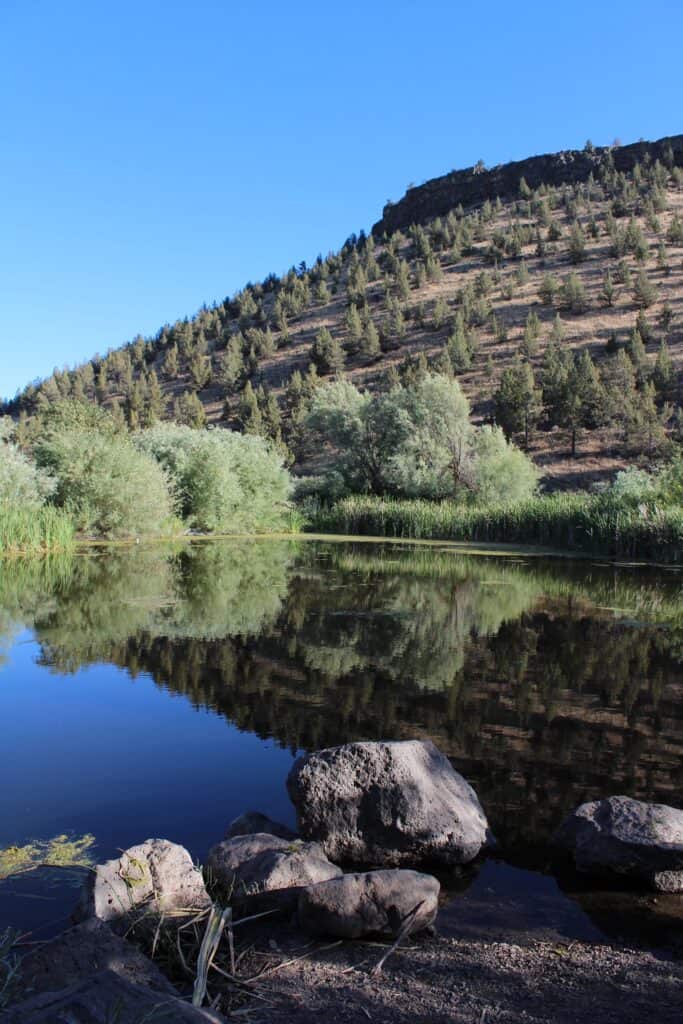 A scenic view of a hill reflecting in prineville youth pond.