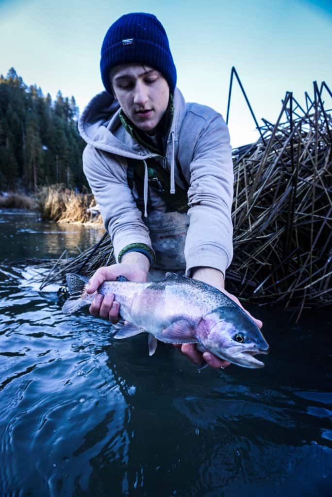 An angler holding a fish with both hands just slightly above the water.