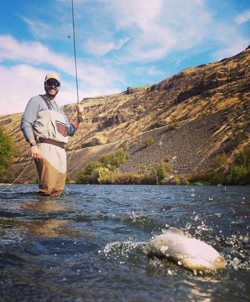 A trout splashes on the line while a fly fisherman smiles at his catch on the Yakima River.