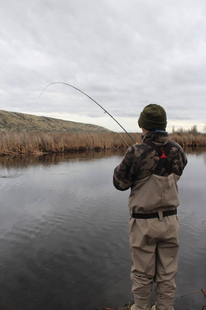 A fly fisherman fighting a large trout on a Rocky Ford Creek, Washington.