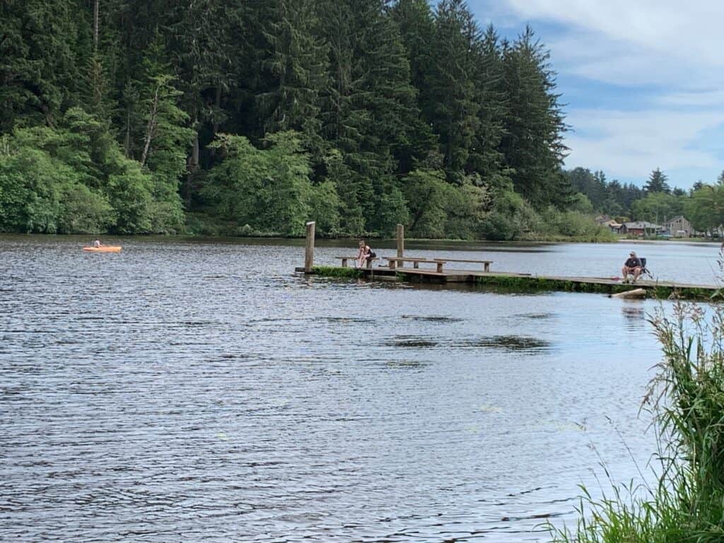 Anglers fishing from a pier at Cullaby Lake on the north Oregon Coast while a kayaker passes by.