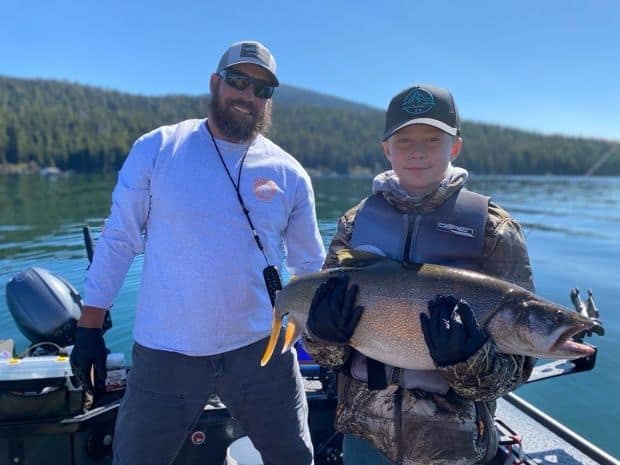 A young angler uses two hands to hold a giant mackinaw trout caught at Odell Lake.