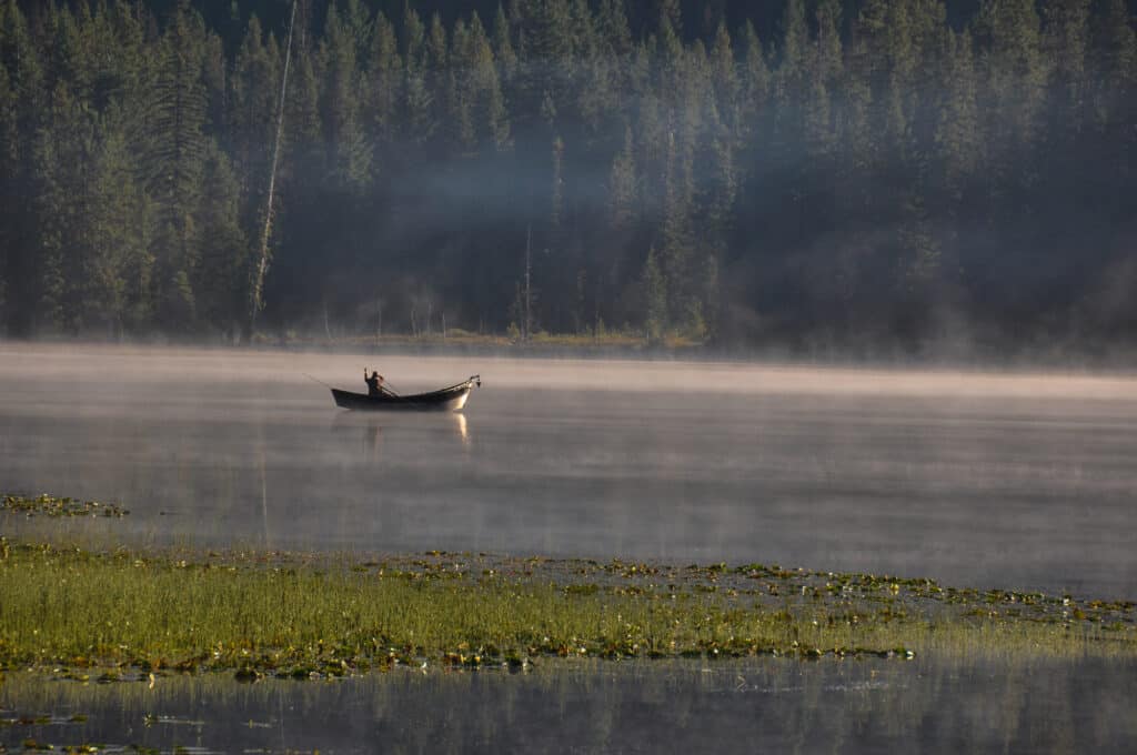 A fisherman in a boat with a scenic view of Trillium Lake near Mount Hood in Oregon.