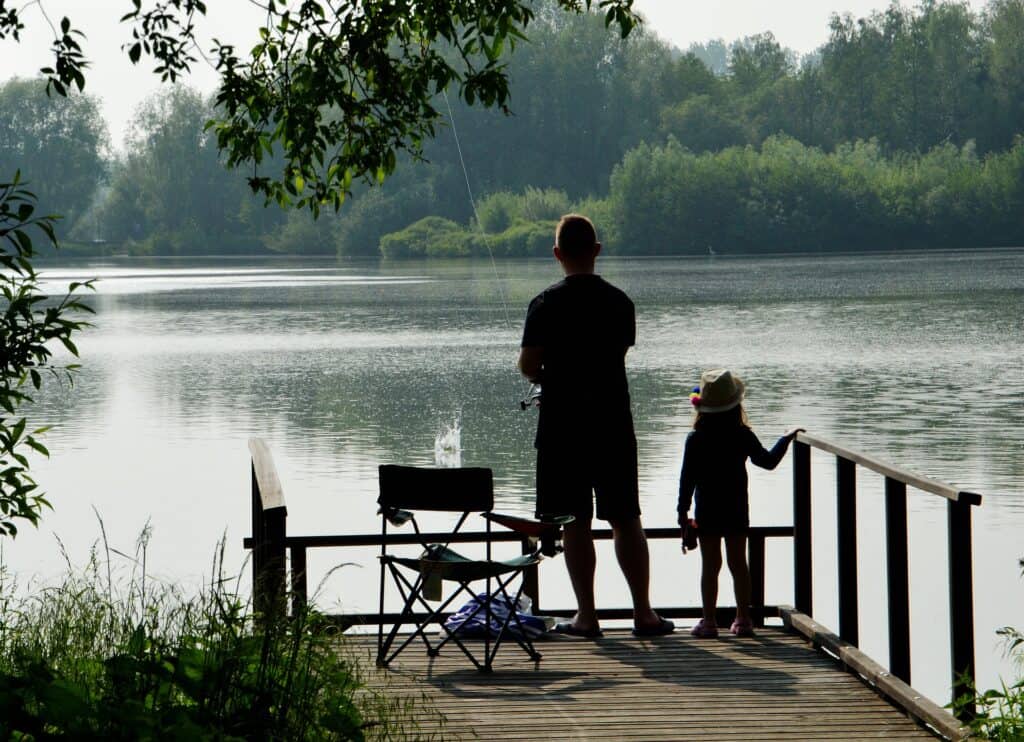 A father and daughter fish from a dock in a lake.