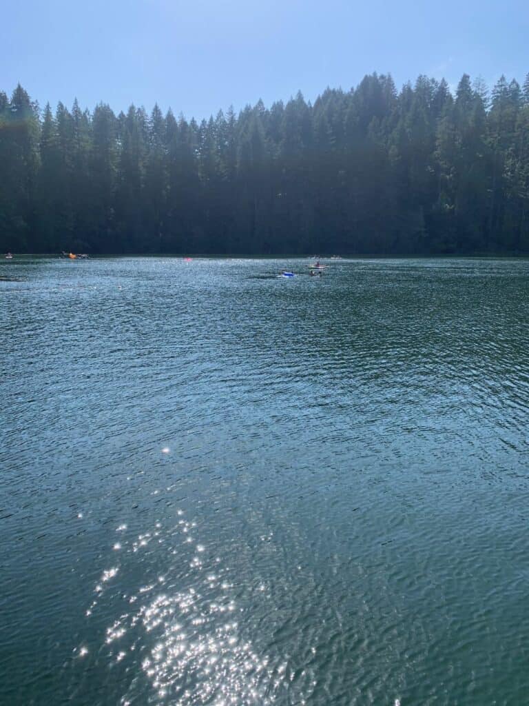 The bright summer sun shimmers across battle ground lake, with kayaks and other small boats in the background.