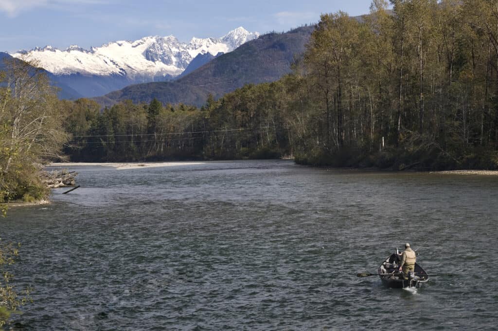 A fishing boat on skagit river with snowy mountains in background.