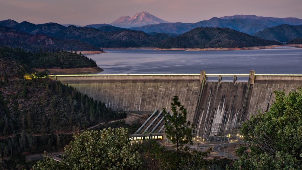 A scenic view of lake shasta with dam in the foreground and mount shasta in the distance.