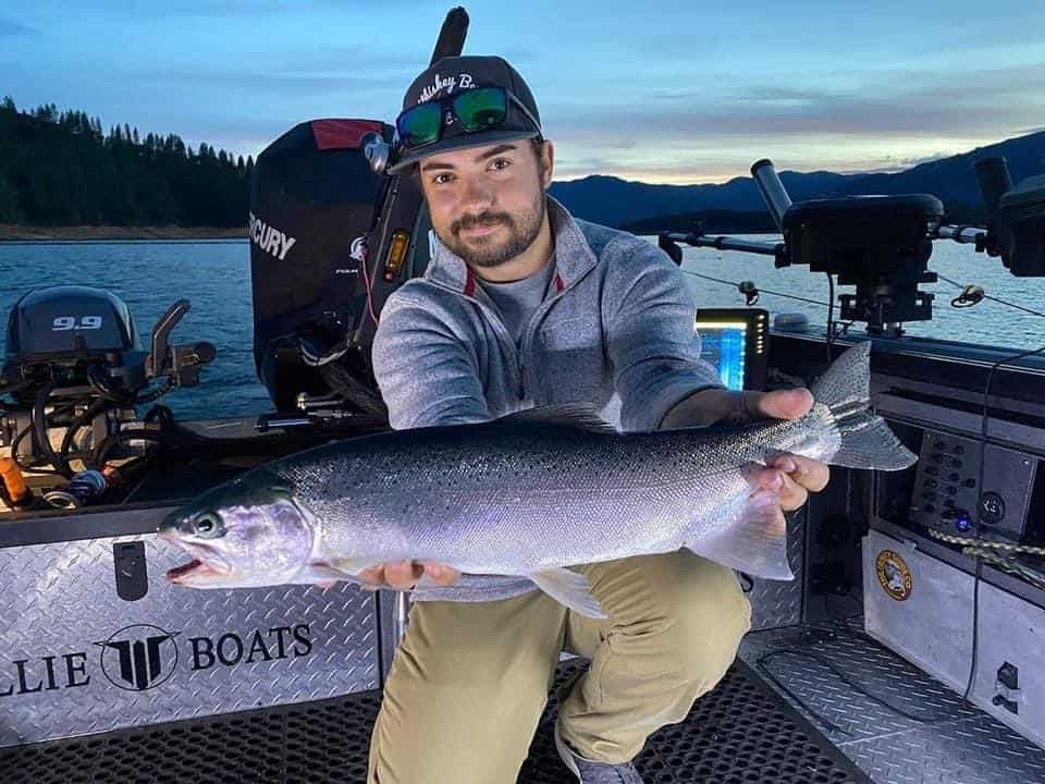 A man in a boat holds a large fish he caught at Lake Shasta, one of California's best fishing lakes.