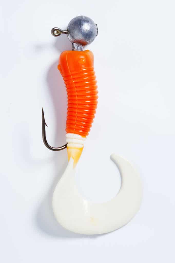 A fishing jig head with a twisty tail orange and white body.