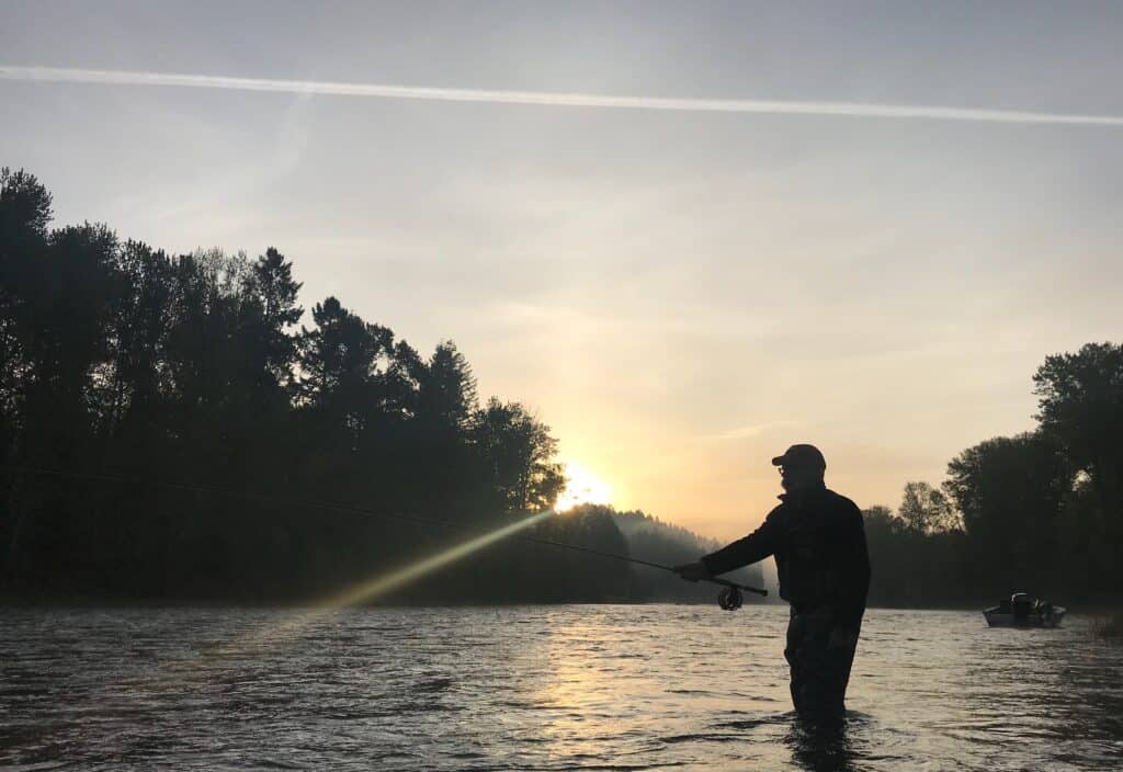 A fly fisherman casts in the clackamas river in silhouette.