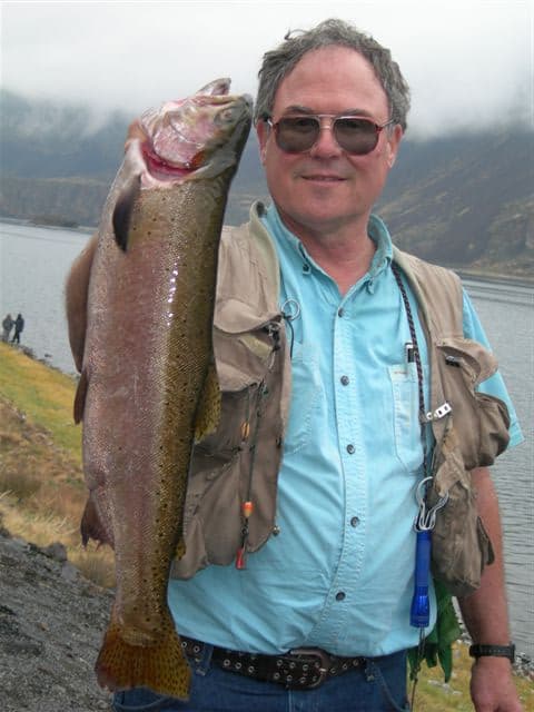 Angler holds a large Lahontan cutthroat trout caught at Lenore Lake, seen in the background.