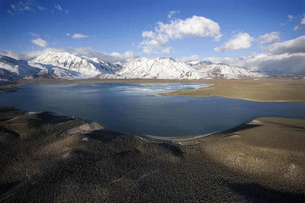 Scenic overview of Crowley Lake in the foreground and snowy mountains in the background.