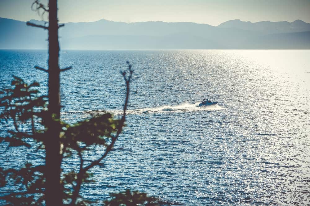 The sun glints off the water of Lake Tahoe while a boat powers across the surface.