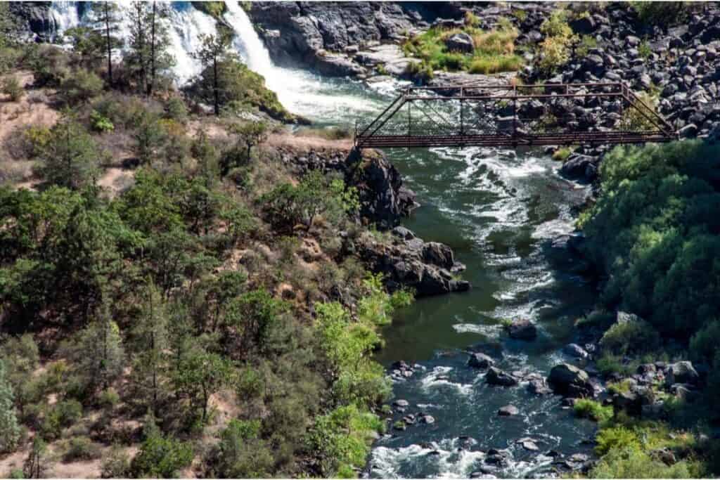 The Pit River tumbles over a small waterfall and under a foot bridge.