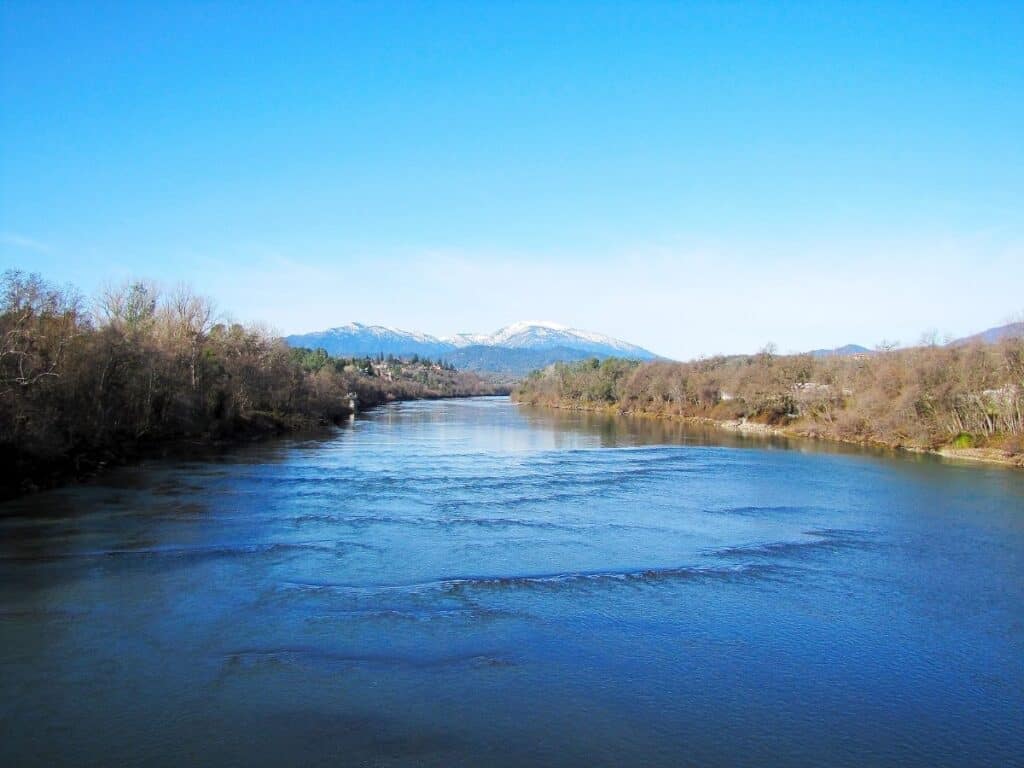 The Sacramento River flows near Redding, California, with snowy mountains in the background.