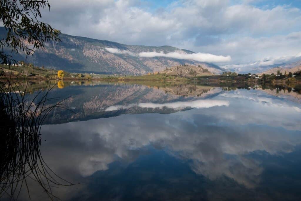 Roses Lake sitting calm with clouds and mountains in the background.