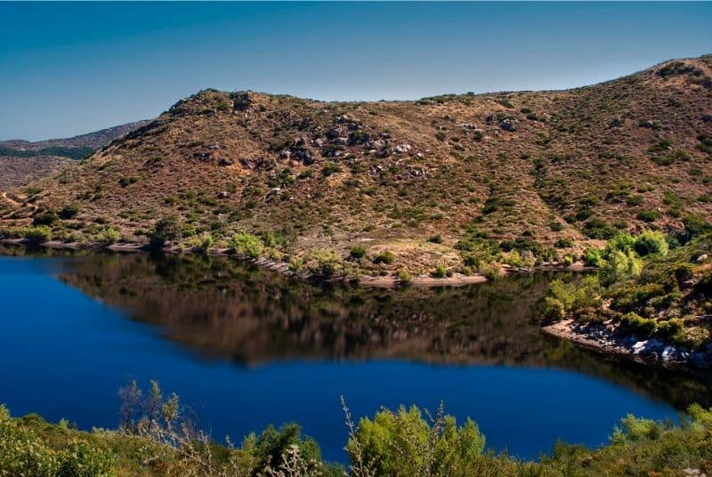 Scenic view of Lake Poway's blue water in front of brown hills.