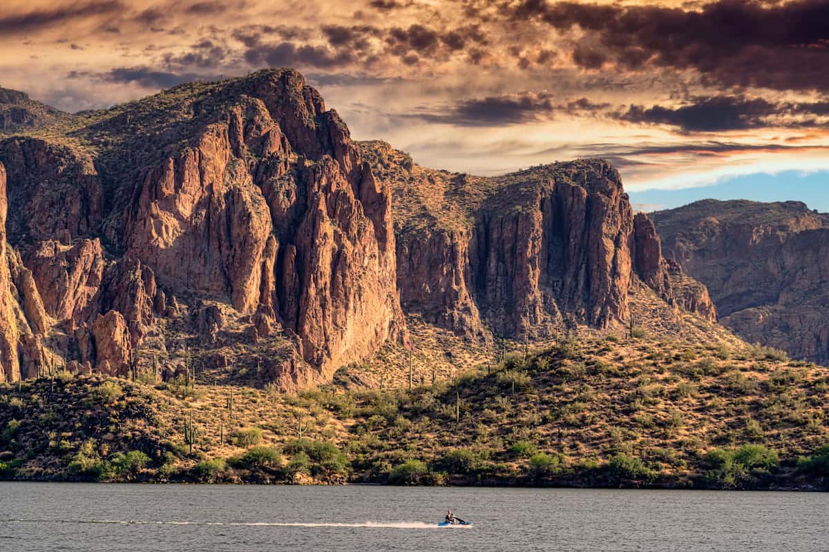 A boat streaks across Saguaro Lake with a huge rock formation in the background.