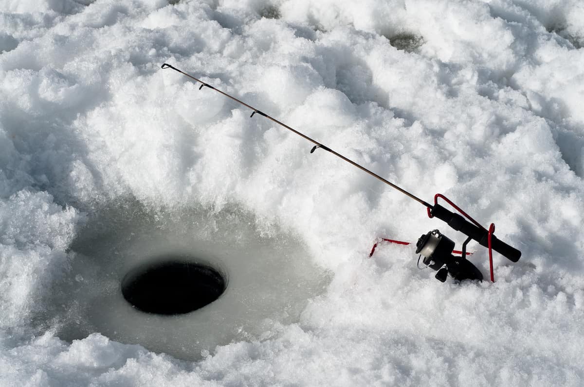 An ice fishing rod with line going into a hole in the ice.