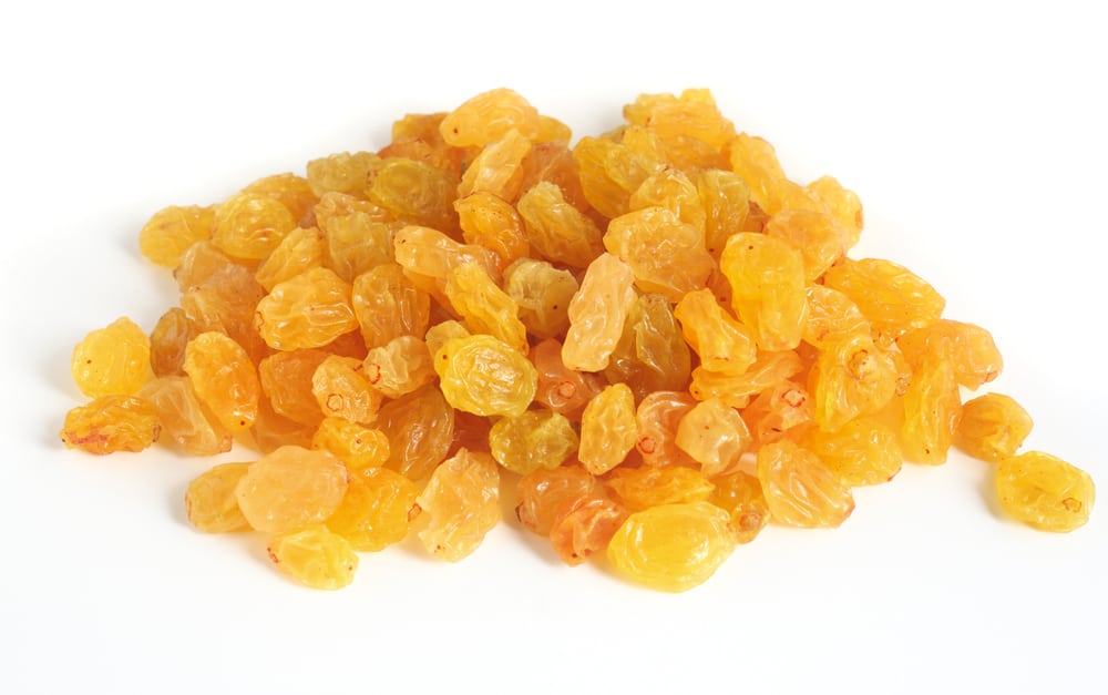 A heap of golden raisins over a white background with light shadows.