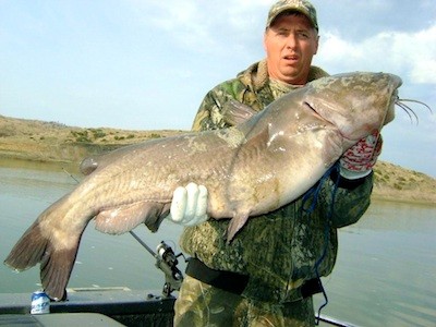 An angler in a boat holds up a mammoth catfish caught in Fort Peck Reservoir in Montana.