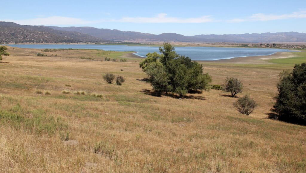 Scenic photo of dry grassland in the foreground and blue Lake Henshaw in the background.