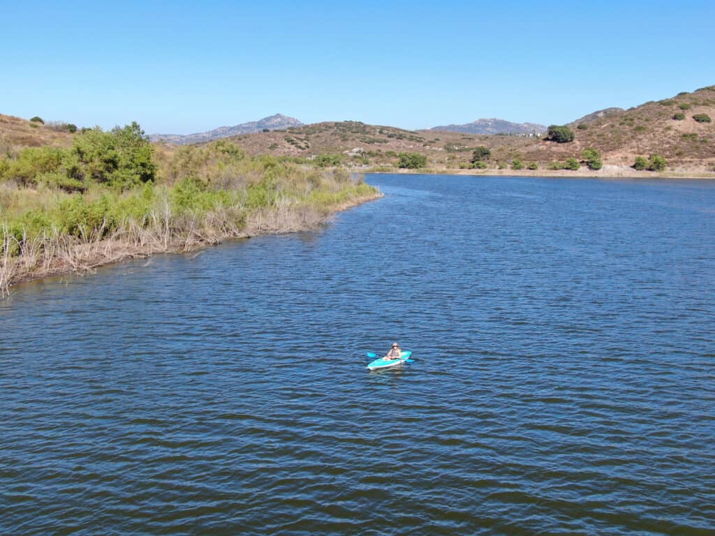 A person in a blue kayak paddles across ripples on the surface of Lake Hodges.