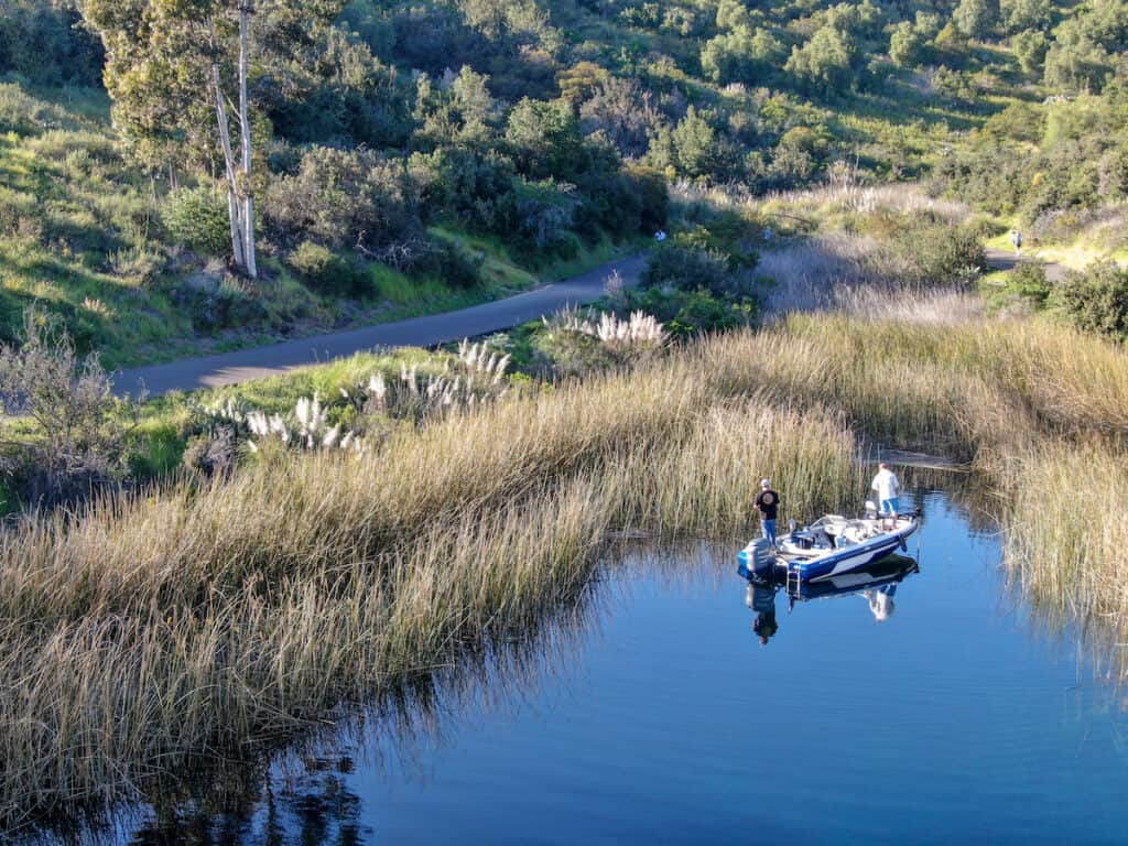 A fishing boat pulled into a small, grass-lined cove with two anglers standing while fishing.