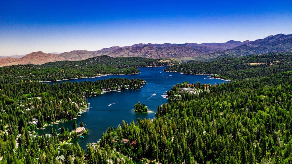 Aerial view of boats speeding along the surface of Arrowhead Lake surrounded by green forest lands and mountains.