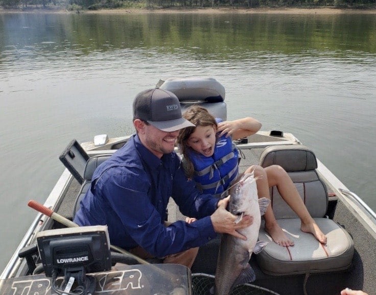 A fisherman holds a huge catfish caught in Oklahoma while a young girl looks on with excitement.