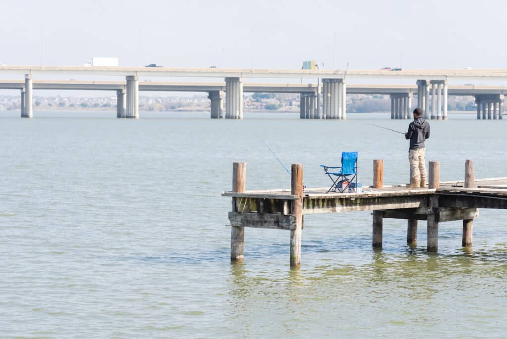 A solitary angler fishing from a pier at Lake Ray Hubbard near Dallas, with a big highway bridge in the background.