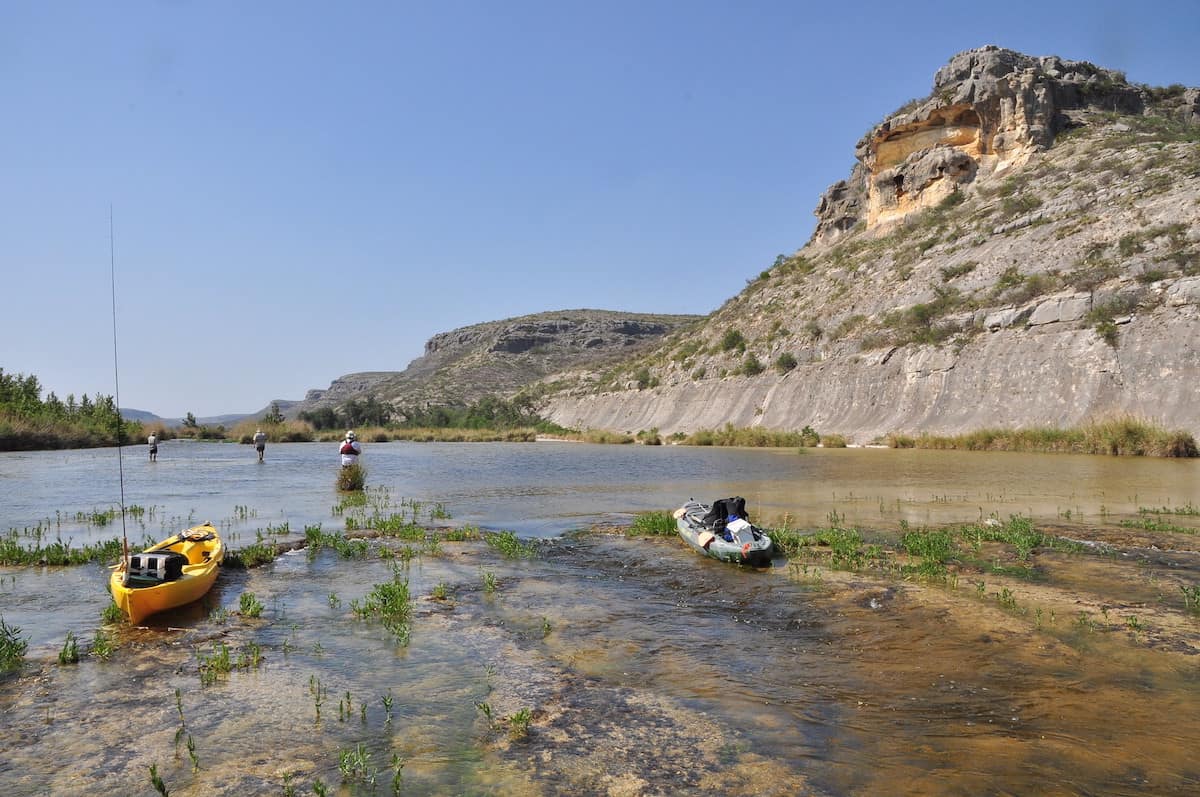 With kayaks parked in the foreground, anglers are fishing in the Devil's River, Texas.