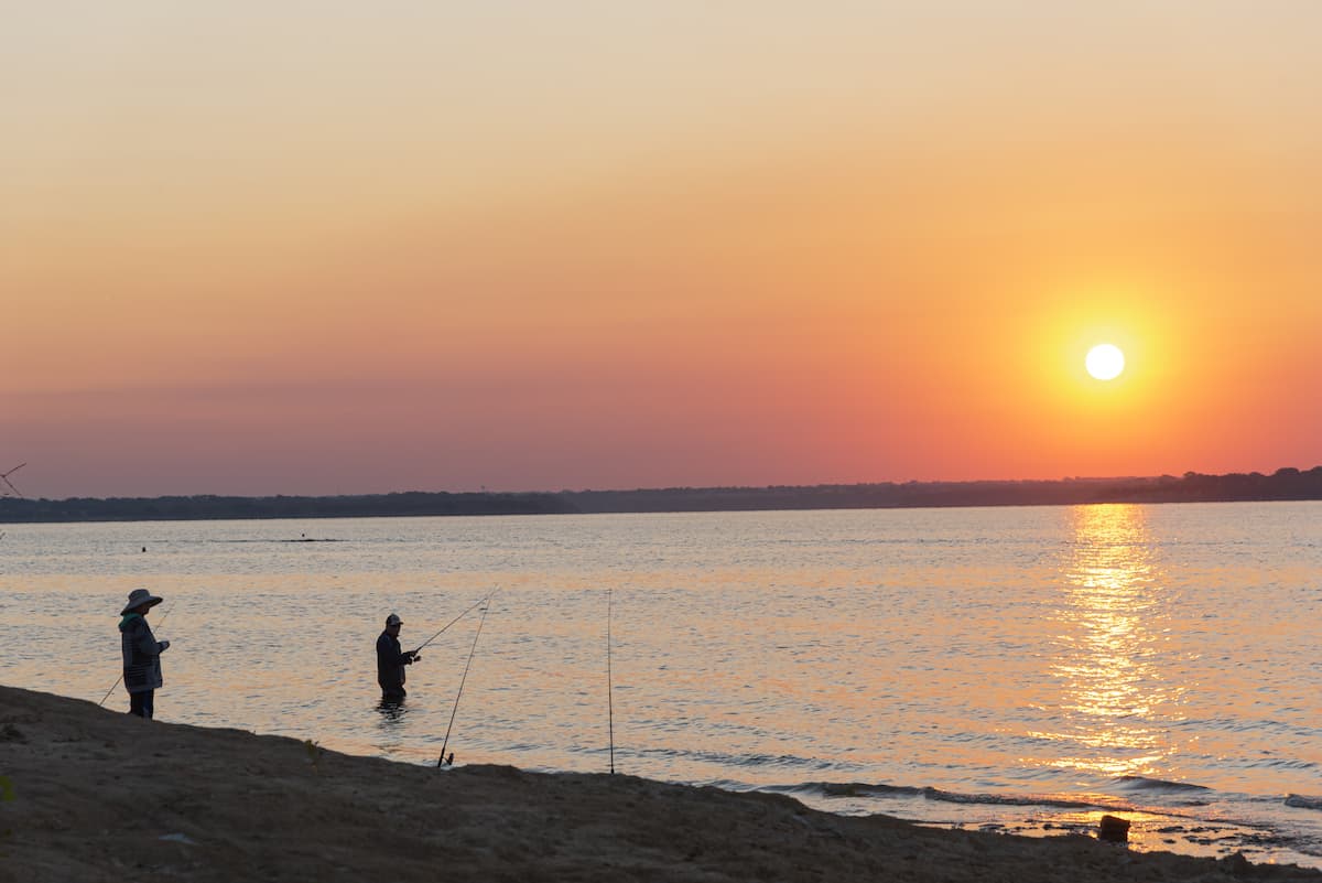 Two anglers fishing at Lake Lavon as the sun rises in the background.