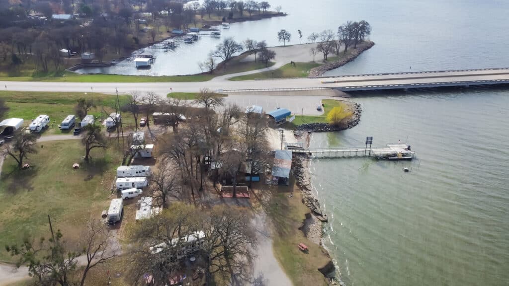 Aerial view of an RV park with a fishing dock near a boat ramp next to Two Mile Bridge over Lake Tawakoni in Quinlan, Texas.